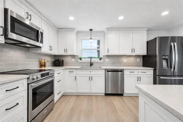 a kitchen with stainless steel appliances granite countertop a stove top oven a refrigerator a sink and dishwasher with white cabinets