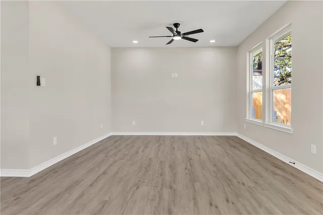 an empty room with wooden floor fan and windows