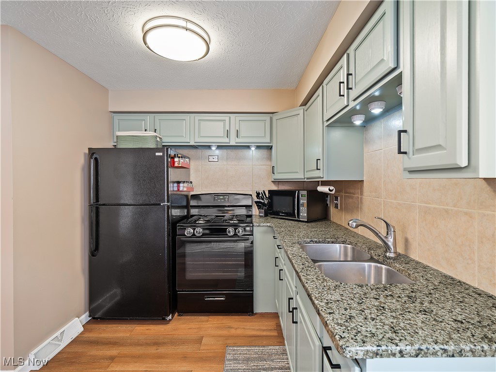 6488 State Road, Unit B5 Cleveland, OH 44134 - Photo 16 of 23 Kitchen with black appliances, sink, light stone counters, light hardwood / wood-style floors, and decorative backsplash