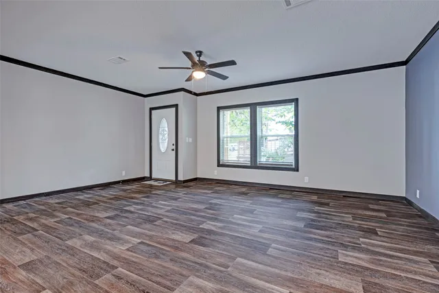 a view of an empty room with wooden floor and a ceiling fan