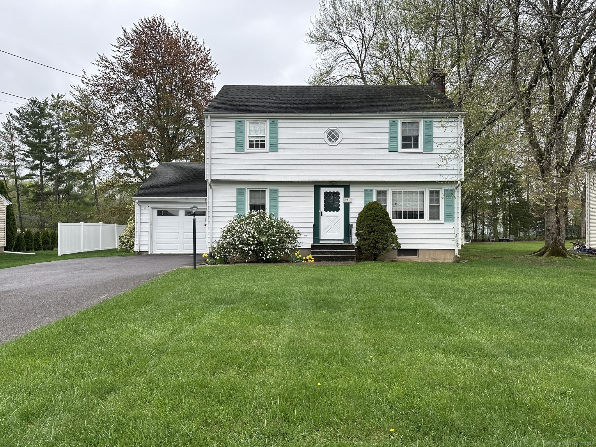 a view of a white house in front of a yard with plants and large trees