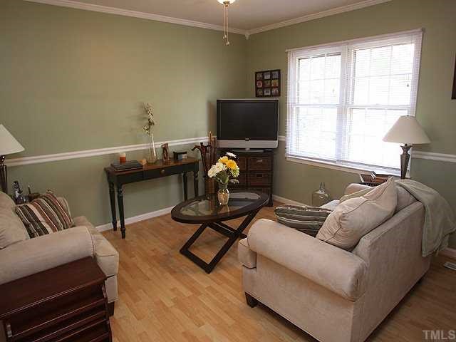 Living room with designer paint, crown molding, chair rail, smooth ceiling, ceiling fan and laminate hardwood floors.