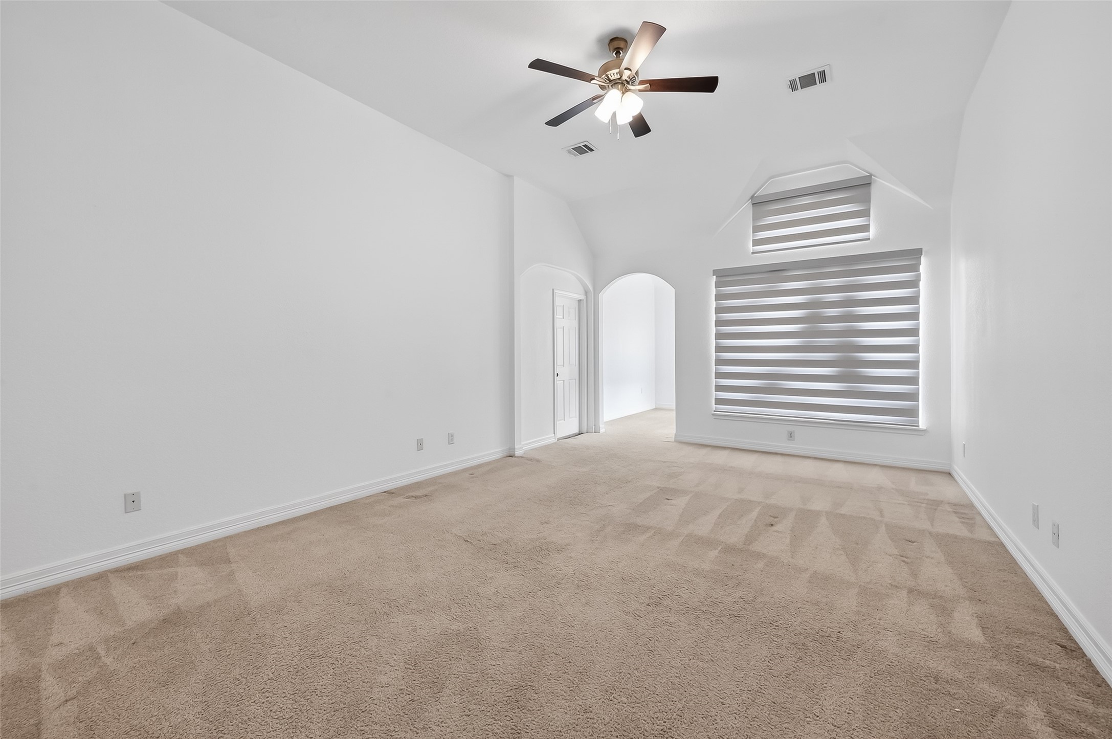 1311 Rene Court Sugar Land, TX 77479 - Photo 18 of 45 Spacious bedroom with neutral carpeting, a ceiling fan, and stylish window shades. The room features an arched doorway leading to another area, offering plenty of natural light and versatility.