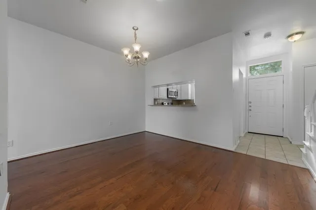 a view of an empty room with chandelier fan and wooden floor