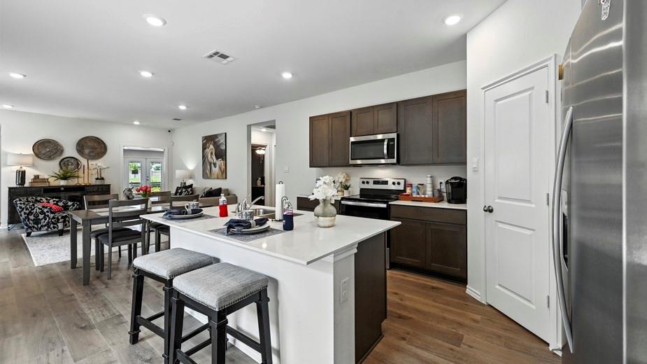 646 Glee Stem Road Lavon, TX 75166 - Photo 5 of 17 Open-concept kitchen featuring a center island with countertop seating, stainless steel appliances, dark wood-finish cabinetry, and wood-finish flooring