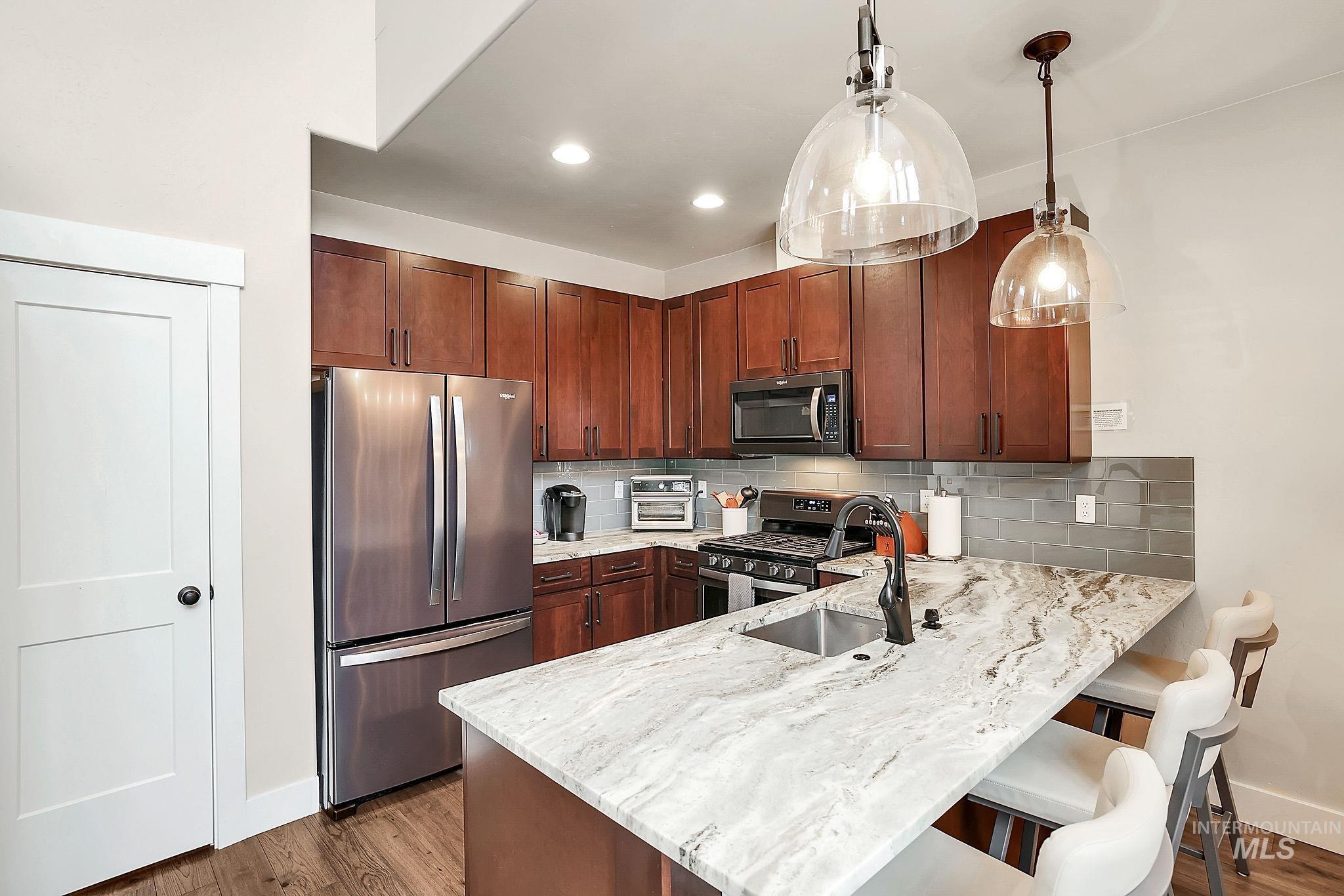 609 Blue Water Circle McCall, ID 83638 - Photo 14 of 45 Kitchen featuring stainless steel appliances, pendant lighting, light stone counters, a breakfast bar area, and a peninsula