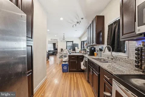 a kitchen with stainless steel appliances granite countertop a refrigerator a sink dishwasher a stove and white countertops with wooden floor