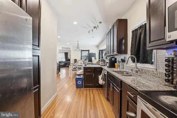 a kitchen with stainless steel appliances granite countertop a refrigerator a sink dishwasher a stove and white countertops with wooden floor