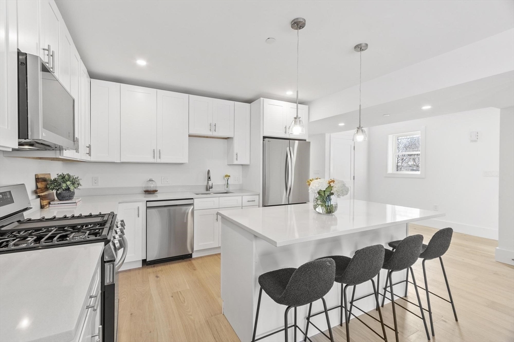 79 Maple Street, Unit 3 Boston, MA 02136 - Photo 4 of 13 a kitchen with stainless steel appliances granite countertop a stove a refrigerator a sink a dining table and chairs with wooden floor