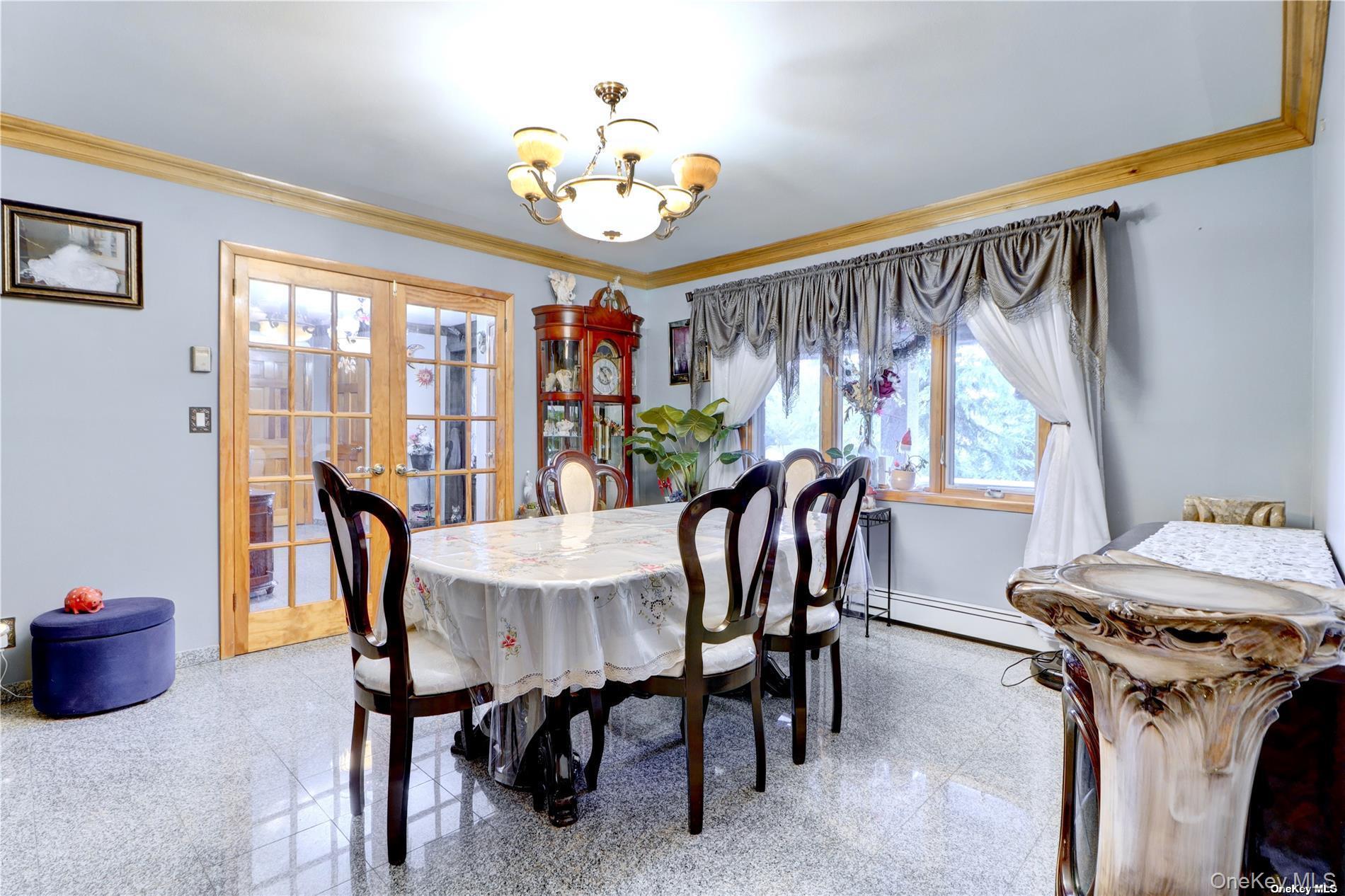 338 Cold Spring Road Syosset, NY 11791 - Photo 4 of 22 Dining space with granite tiled floors, french doors, a chandelier, crown molding, and a baseboard radiator