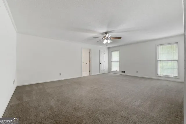 an empty room with chandelier fan and windows