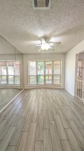 an empty room with wooden floor fan and windows