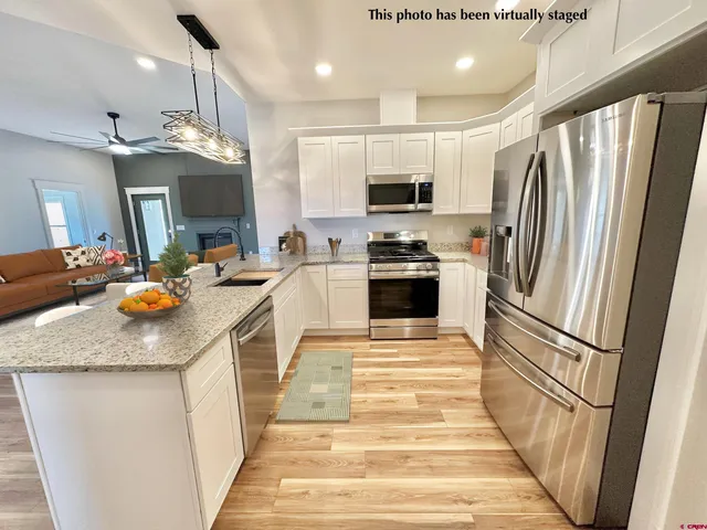 a kitchen with stainless steel appliances granite countertop a refrigerator a stove a sink dishwasher a refrigerator and a dining table with wooden floor