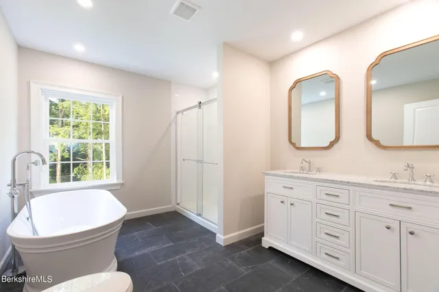 a bathroom with double vanity sink a mirror a toilet and a window