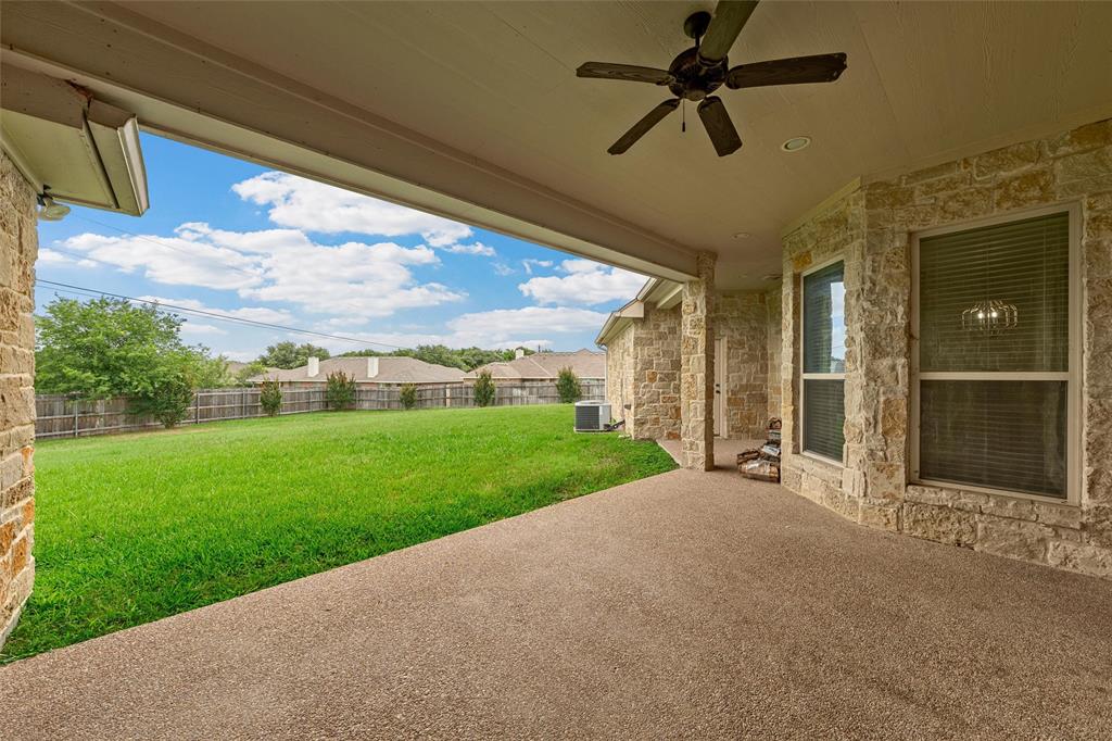 144 Ellis Farm Road Hewitt, TX 76643 - Photo 34 of 36 Expansive covered patio with exposed aggregate flooring, featuring an outdoor ceiling fan with integrated lighting