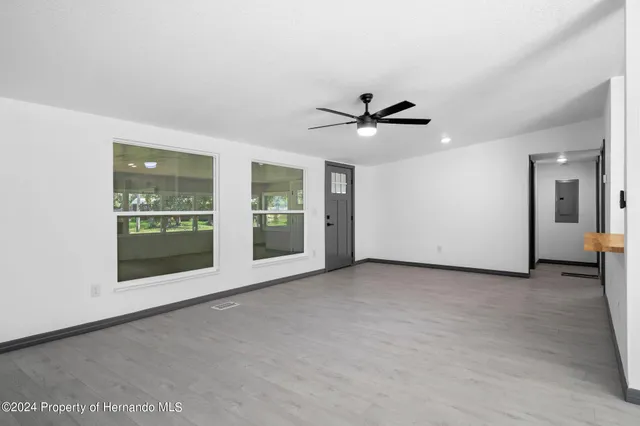 an empty room with chandelier fan and windows
