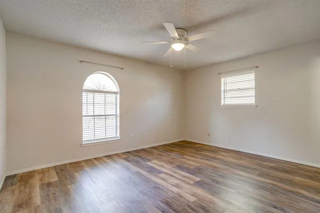 an empty room with wooden floor chandelier fan and windows