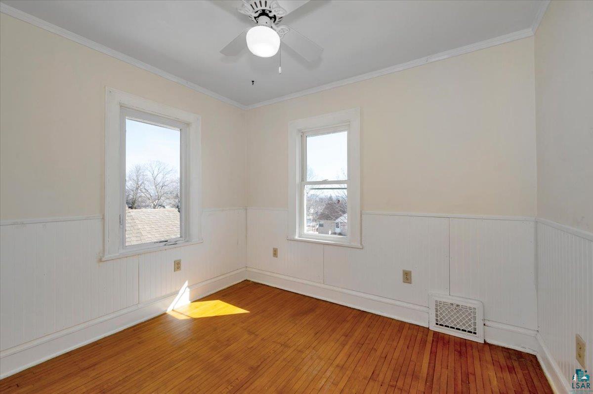 4345 West 8th Street Duluth, MN 55807 - Photo 25 of 31 Empty room featuring hardwood / wood-style flooring, a wainscoted wall, crown molding, a ceiling fan, and healthy amount of natural light