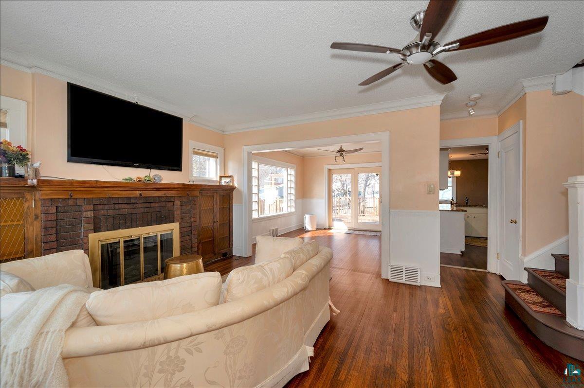 4345 West 8th Street Duluth, MN 55807 - Photo 6 of 31 Living area featuring dark wood finished floors, a ceiling fan, a fireplace, crown molding, and a textured ceiling