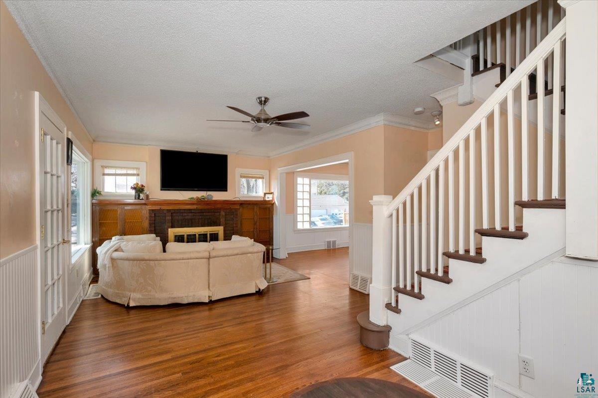 4345 West 8th Street Duluth, MN 55807 - Photo 7 of 31 Living room with wainscoting, ceiling fan, wood finished floors, a brick fireplace, and crown molding