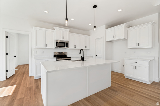 1351 Maple Circle Santaquin, UT 84655 - Photo 13 of 42 Modern kitchen featuring a large central island with a sink, white cabinetry with dark hardware, stainless steel appliances, quartz countertops, and wood-finish flooring