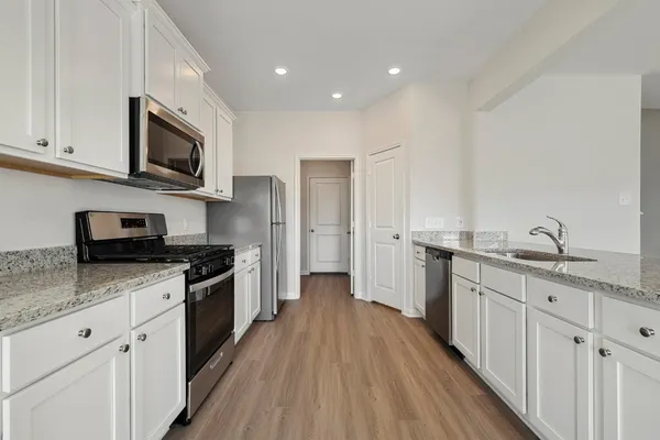 a kitchen with stainless steel appliances granite countertop a stove top oven a sink dishwasher and a refrigerator with wooden floor