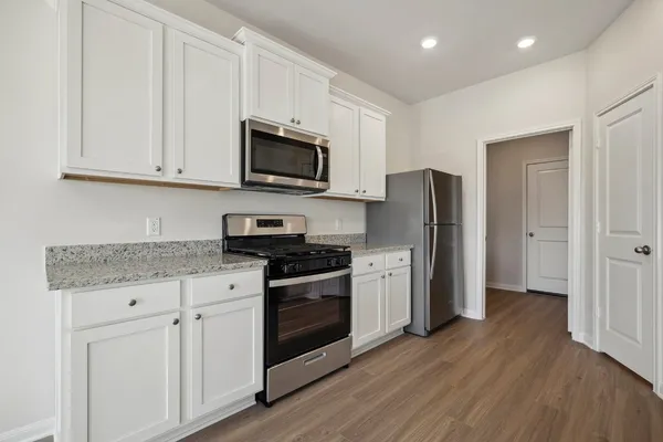 a kitchen with stainless steel appliances granite countertop a refrigerator stove a sink and white cabinets with wooden floor