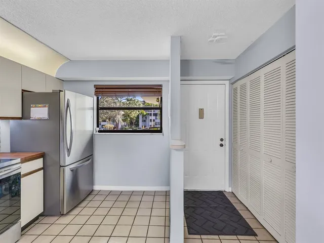 a view of a refrigerator in kitchen and an empty room in wooden floor