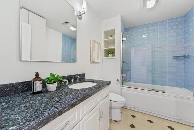 a bathroom with a granite countertop sink a toilet a mirror and shower