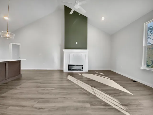 an empty room with wooden floor chandelier fan and windows