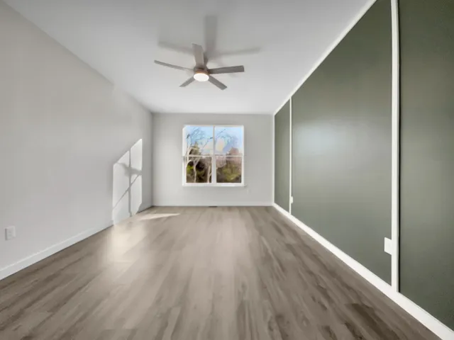 an empty room with wooden floor fan and windows