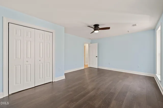 a view of an empty room with wooden floor and a kitchen