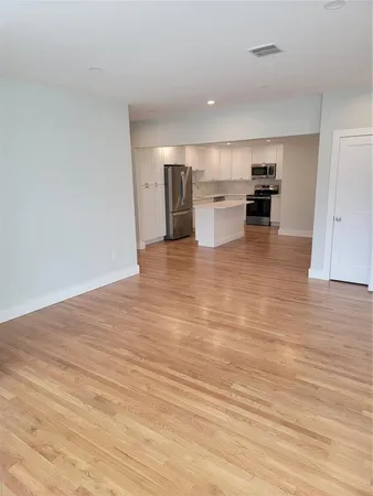 a view of kitchen and empty room with wooden floor
