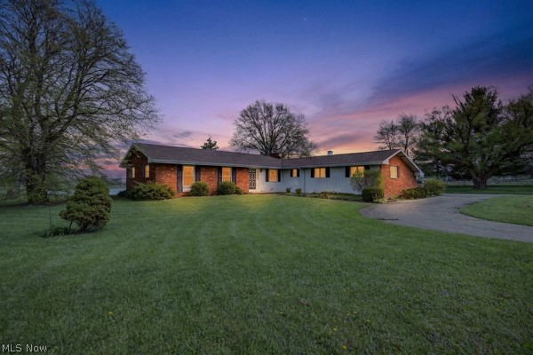 Ranch-style residence featuring a brick and light-colored siding exterior, dark shingle roof, and a mature tree canopy