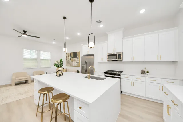 a kitchen with stainless steel appliances a stove a sink a refrigerator a center island a dining table and chairs