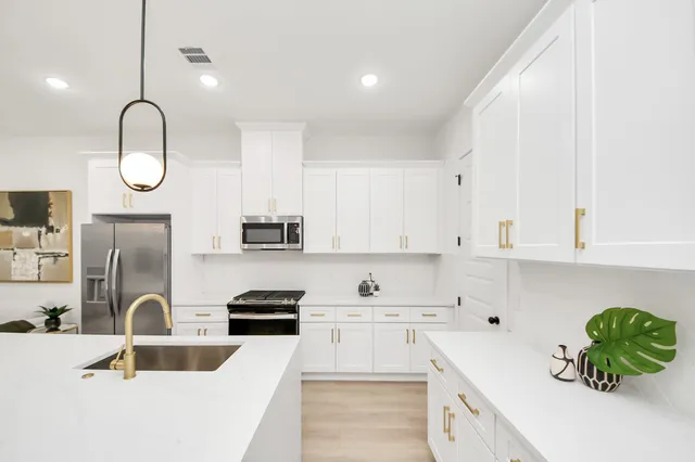 a kitchen with stainless steel appliances granite countertop a sink a stove and white cabinets with wooden floor