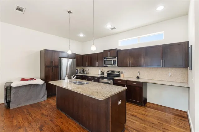 a kitchen with stainless steel appliances a sink a stove a refrigerator cabinets and wooden floor