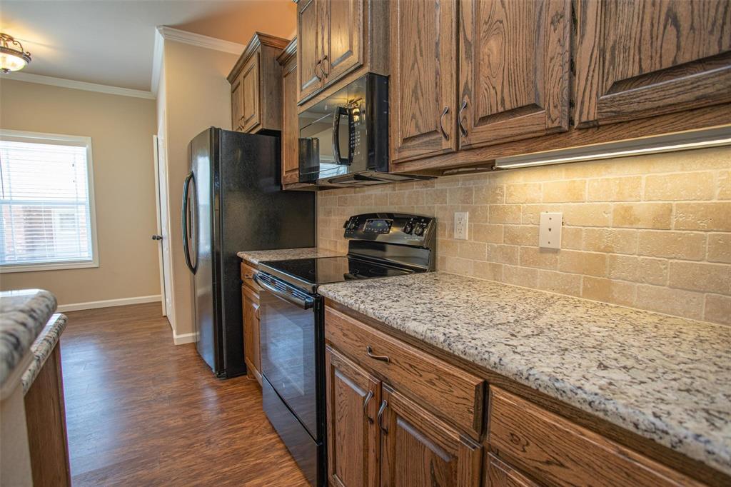 455 Neals Hill Road Oak Ridge, TX 76240 - Photo 12 of 19 Kitchen with black appliances, crown molding, light stone countertops, brown cabinetry, and dark wood-type flooring