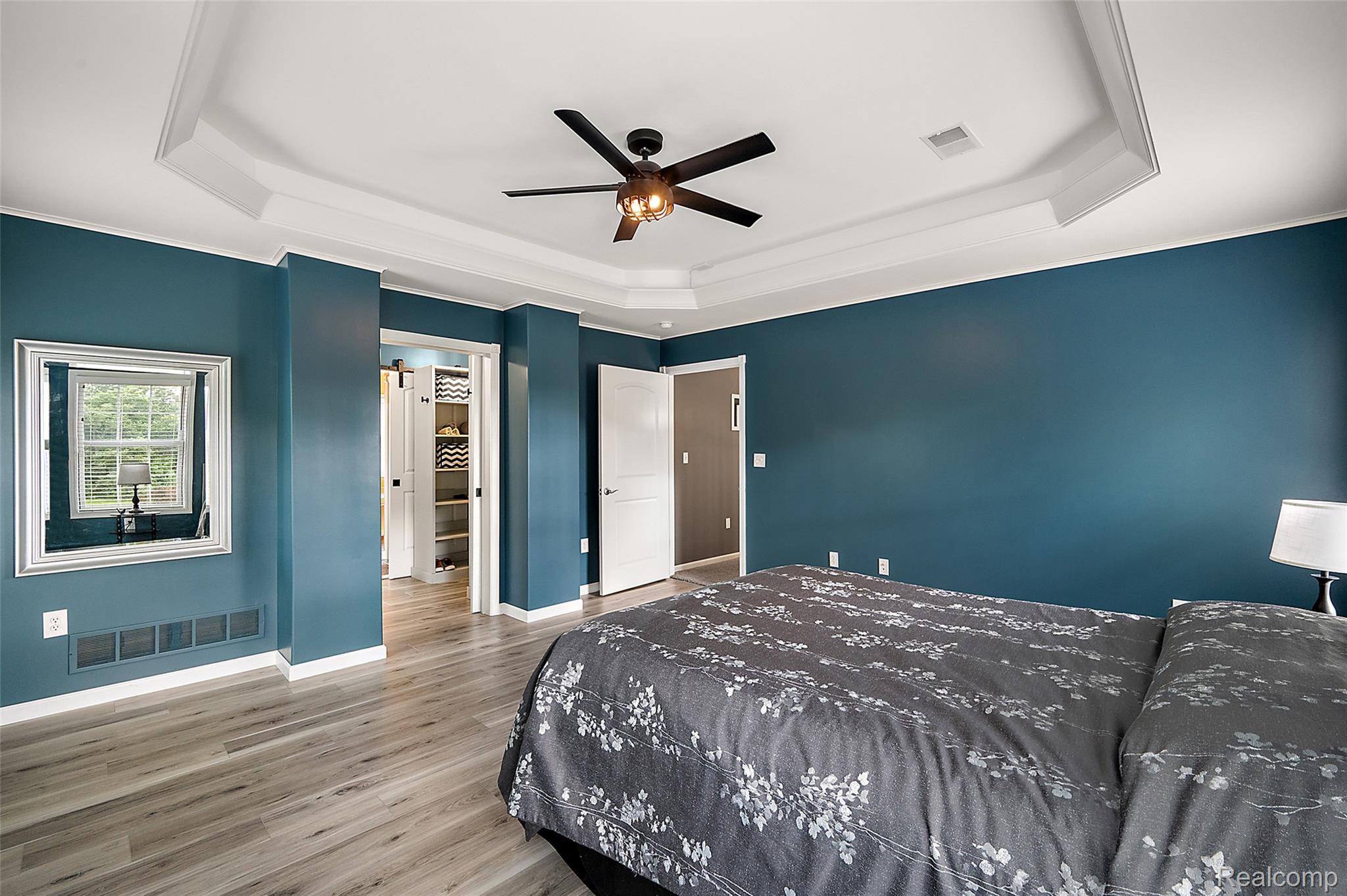 5035 Hidden Ridge Road Metamora, MI 48455 - Photo 29 of 65 Room featuring a tray ceiling with a dark-tone ceiling fan, light wood-finish flooring, white baseboards, and a doorway revealing built-in shelving