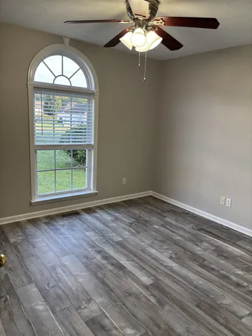 an empty room with wooden floor fan and a window