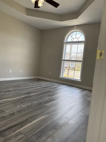 an empty room with wooden floor fan and windows