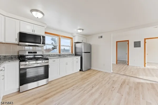 a kitchen with stainless steel appliances a stove top oven a sink dishwasher and a refrigerator with wooden floor