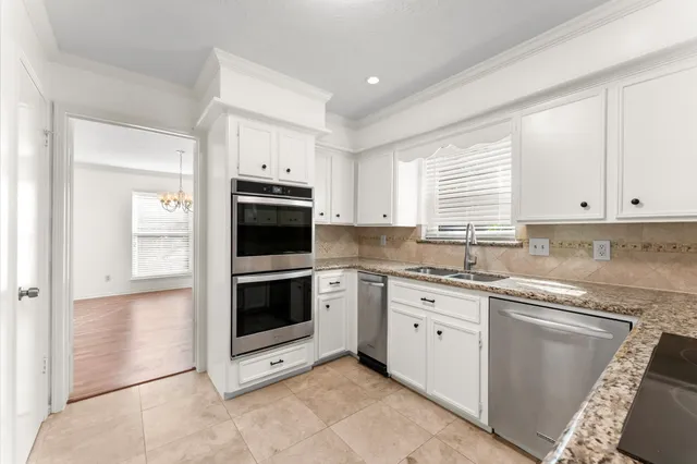 a kitchen with granite countertop white cabinets a sink and dishwasher next to a window
