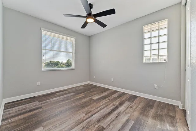 an empty room with wooden floor ceiling fan and windows