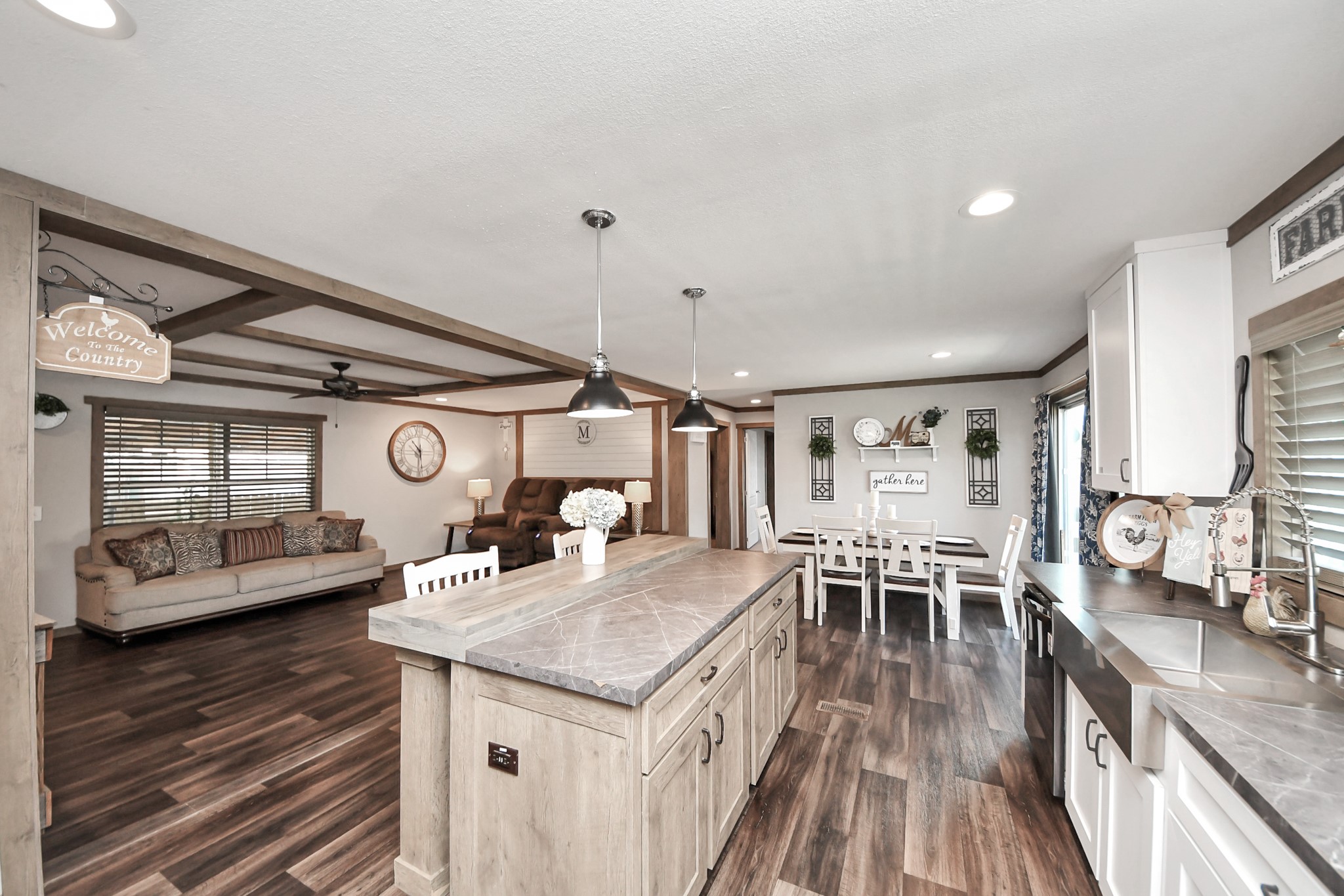 131 Kiowa Court Rosharon, TX 77583 - Photo 1 of 42 This open-concept living space features a spacious kitchen with a large island, modern lighting, and ample cabinetry. It flows into a cozy living area with a sofa and dining space, all accented by wood-look vinyl flooring and rustic decor.