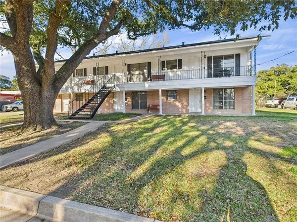 a view of a white house next to a yard with potted plants and large trees