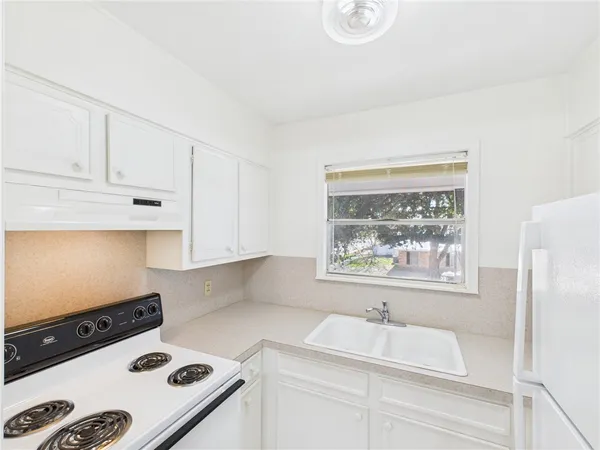 a kitchen with a white stove top oven and white countertops with wooden floor