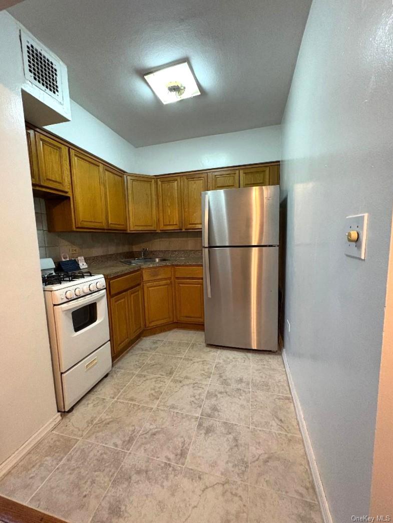 41-31 51st Street, Unit 6M Queens, NY 11377 - Photo 5 of 23 Kitchen featuring white gas range oven, freestanding refrigerator, brown cabinetry, tasteful backsplash, and light tile patterned floors