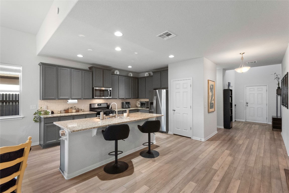 932 Medina Way Leander, TX 78641 - Photo 9 of 28 Kitchen featuring gray cabinetry, a breakfast bar, light stone countertops, appliances with stainless steel finishes, and an island with sink