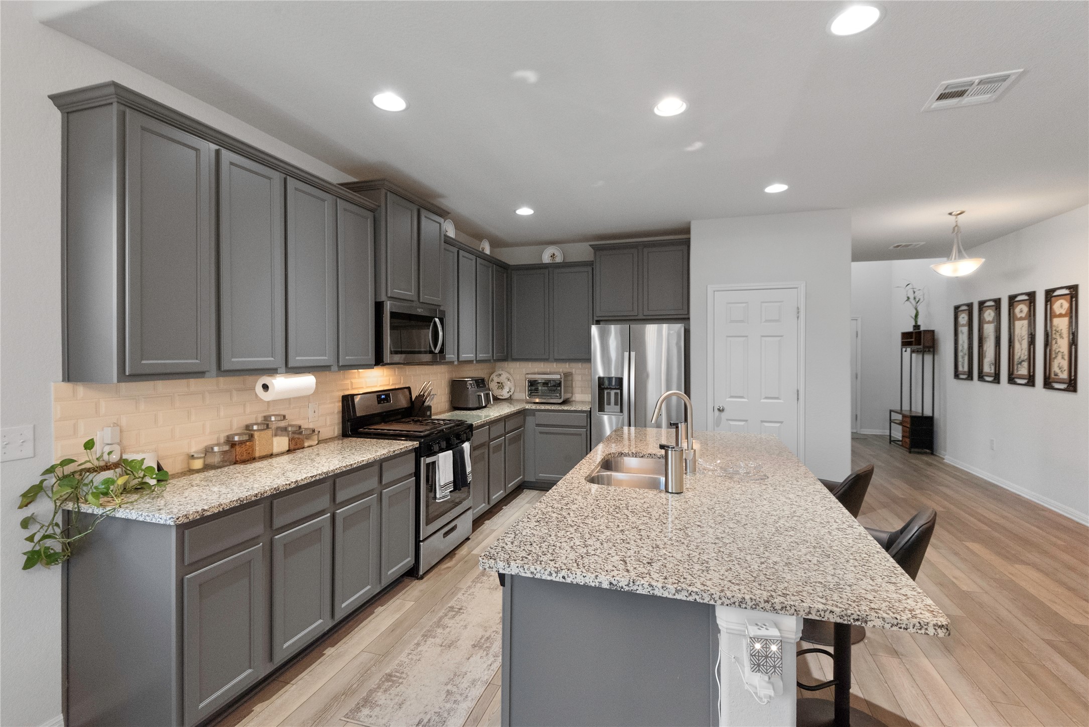 932 Medina Way Leander, TX 78641 - Photo 8 of 28 Kitchen with gray cabinets, a kitchen bar, stainless steel appliances, tasteful backsplash, and light stone countertops